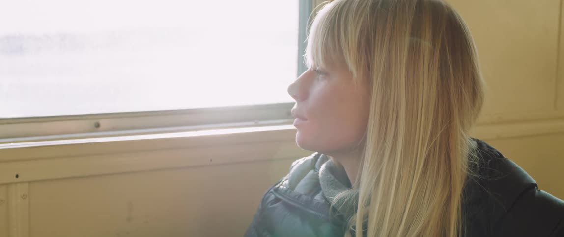 A woman in a winter coat looks out the window of the passenger ferry she's traveling on