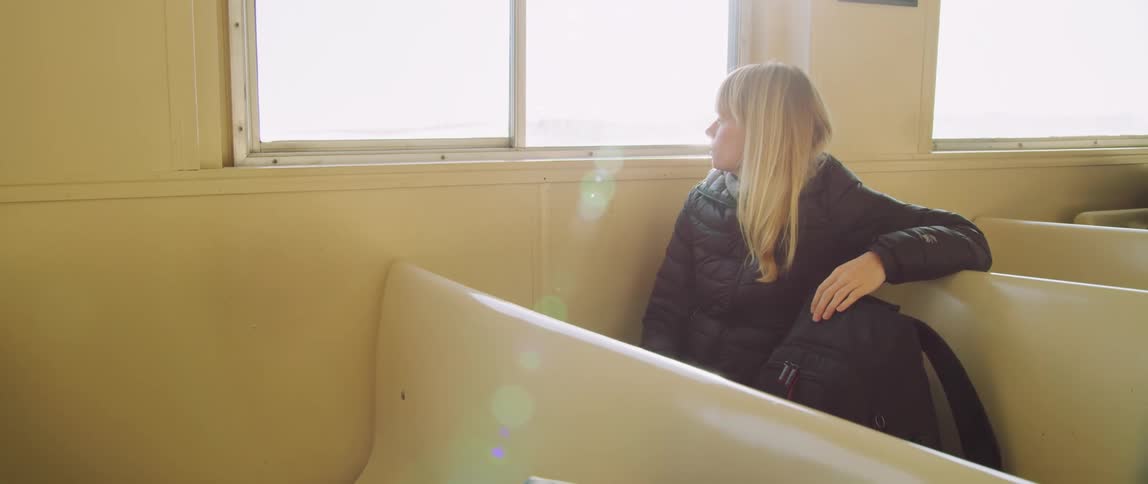 A woman in a black coat takes a seat by a window in a passenger ferry