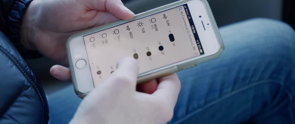 A woman scrolls through her weather app on her phone