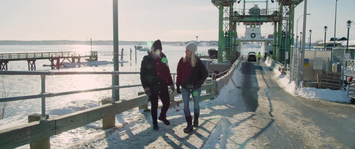 A woman arrives on shore and is greeted by a friend during a winter trip