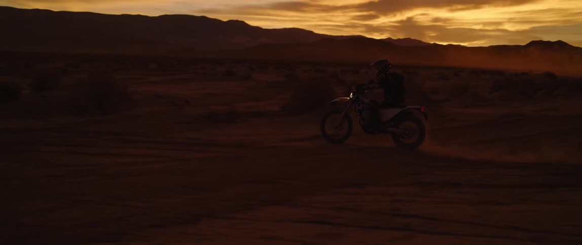 Motorcyclist rides a motorbike in a field at night and jumps it over a small hill