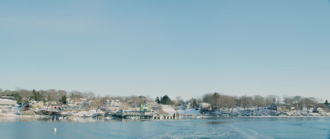 A ship pulls away from a small coastal village covered in snow