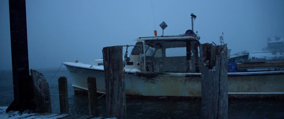 A small fishing boat stays tethered to a dock during a snow storm