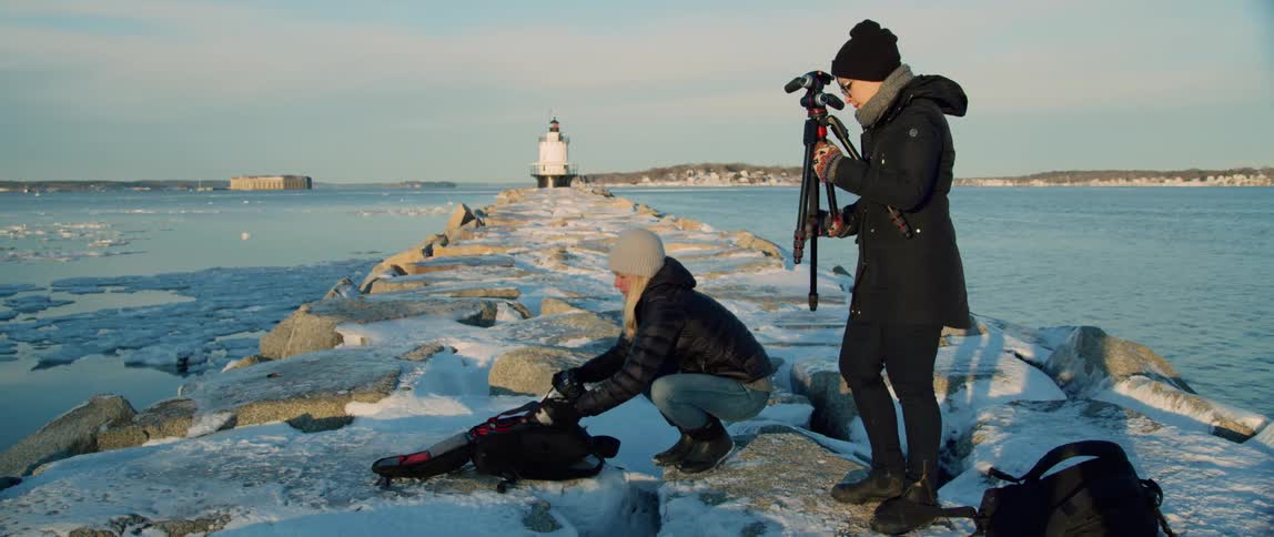 Photographers set up a camera on a breakwater by a lighthouse in winter