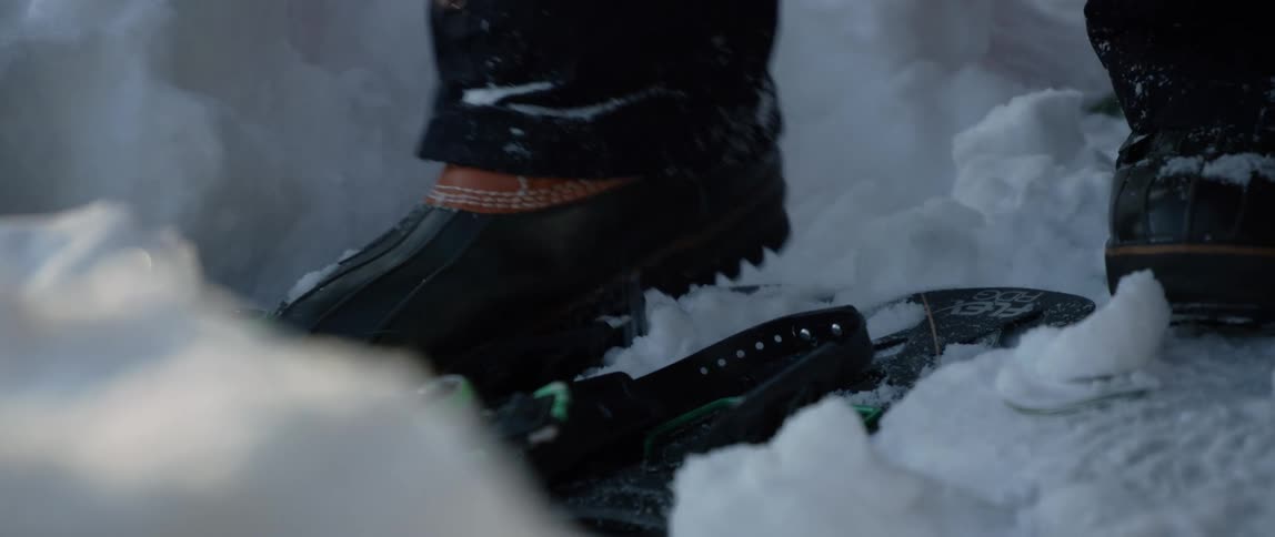 A man lays down snowshoes and then places his boots into them