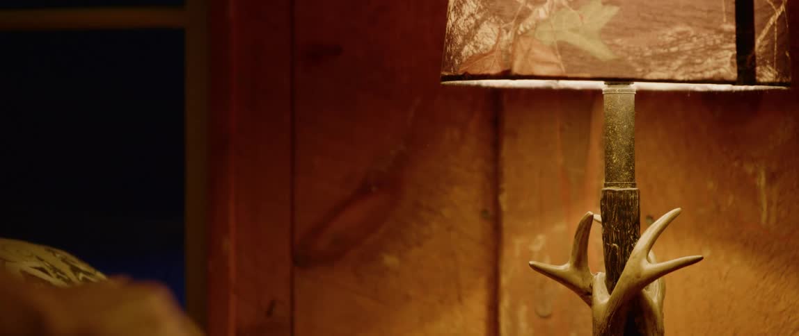 A man turns on a lamp in a rustic cabin on a cold winter morning