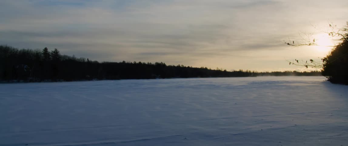 The first light of a wintery day shines on a snowy wind swept frozen lake
