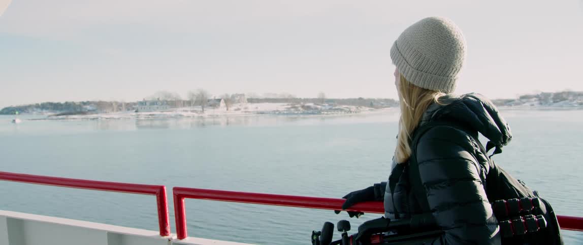 A woman looks out over the bow of a ship to see a coastline covered in snow