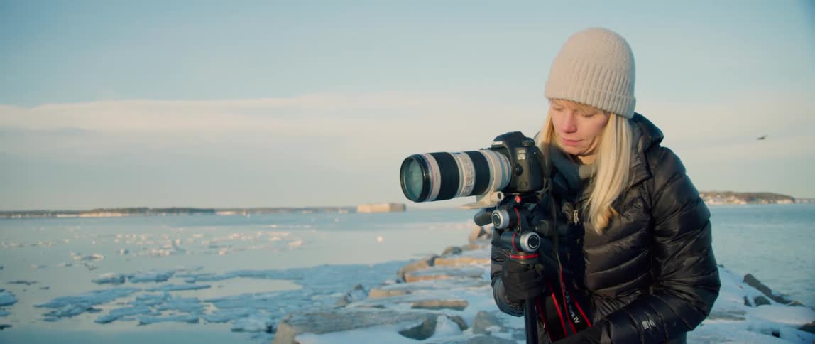 A female photographer adjusts her camera along a wintery coastline