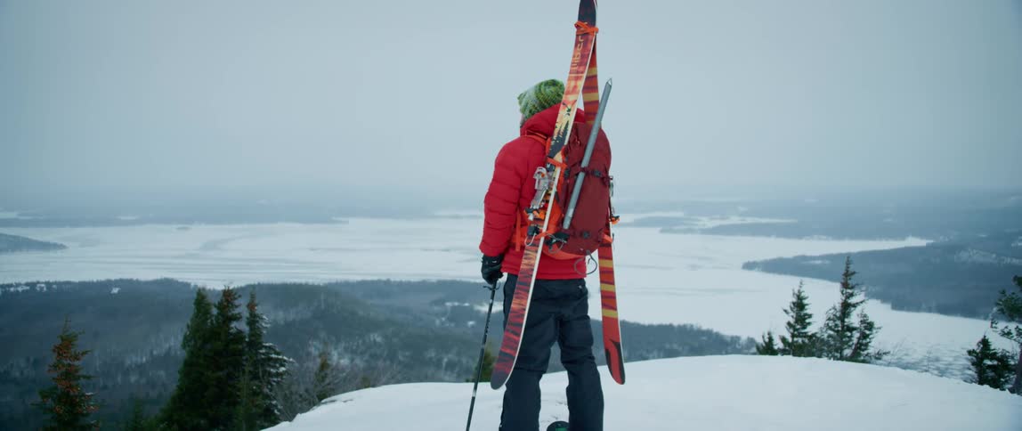 A skier hikes to the summit of a mountain overlooking a frozen panoramic below