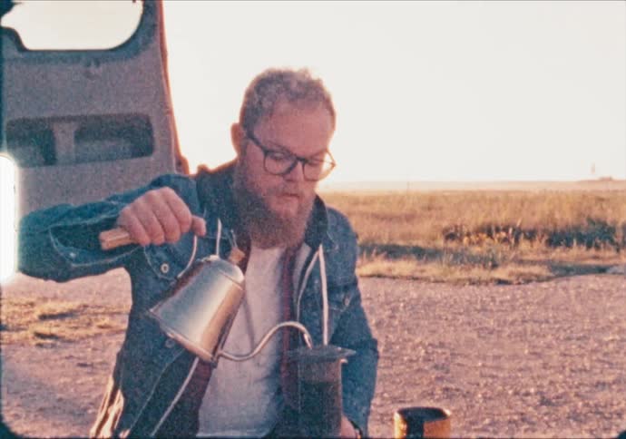 A bearded man makes coffee at a camp site