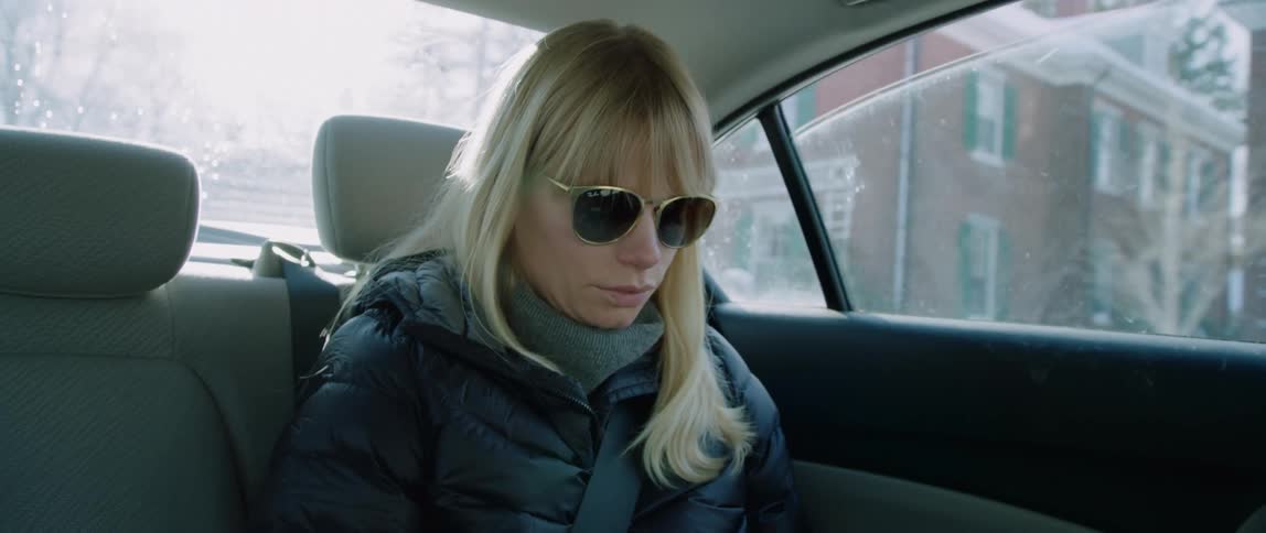 A woman sits in the back of a car as it drives through a snow covered neighborhood