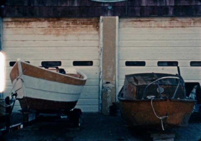 Two small fishing boats sit on trailers in front of a garage