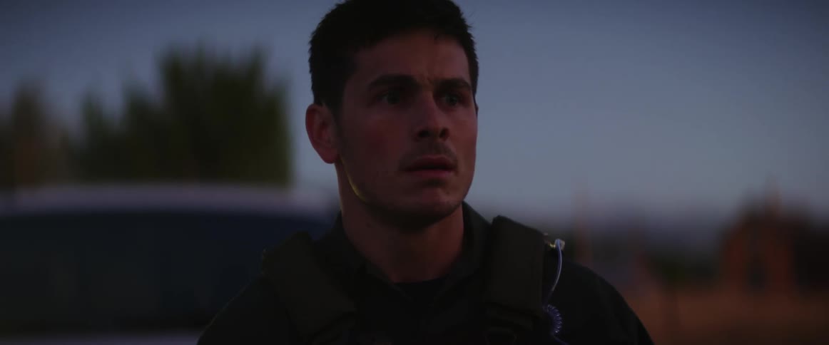 A police officer in a tactical vest stands outdoors with a shocked expression on his face