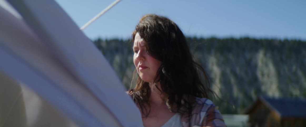 Females removes clothes pins from laundry that is hanging outside to dry on the clothesline and places the clothes in a basket as a gentle breeze blows