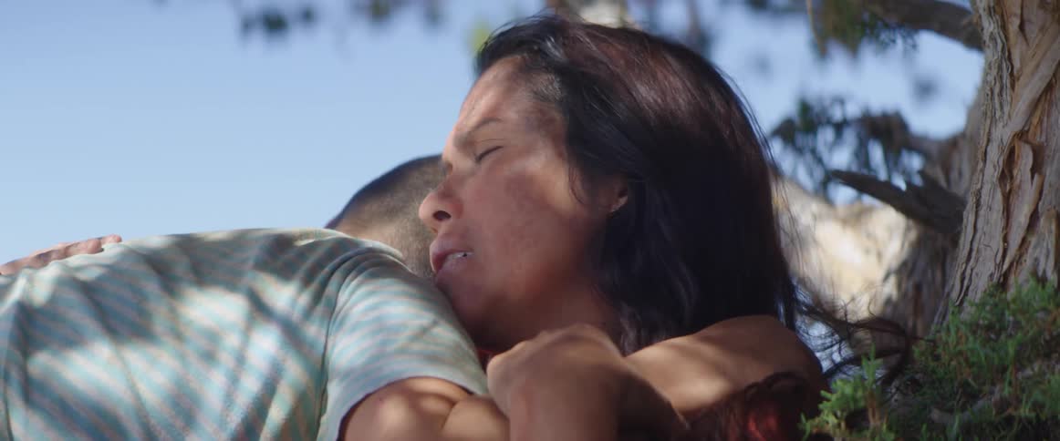 A child hugs a distressed woman sits on the ground against a tree