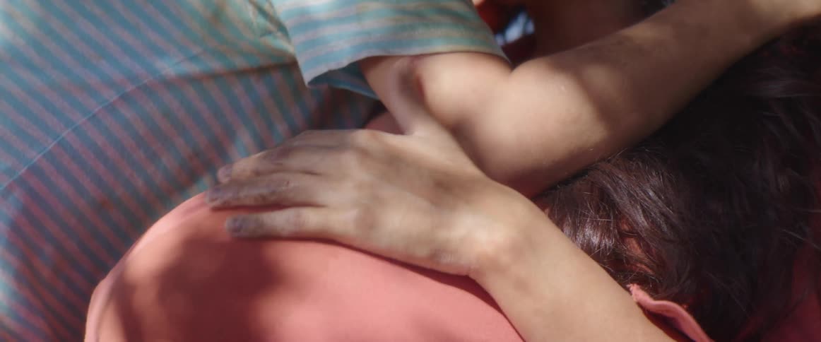 A girl calls her brother in and hugs him as they both hug their mother
