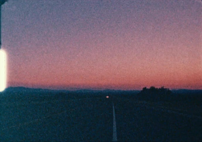 A lone vehicle drives along a long desert road at sunset
