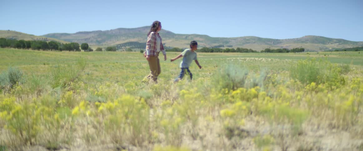 Mother and son holding hands walk in an open field on a windy day