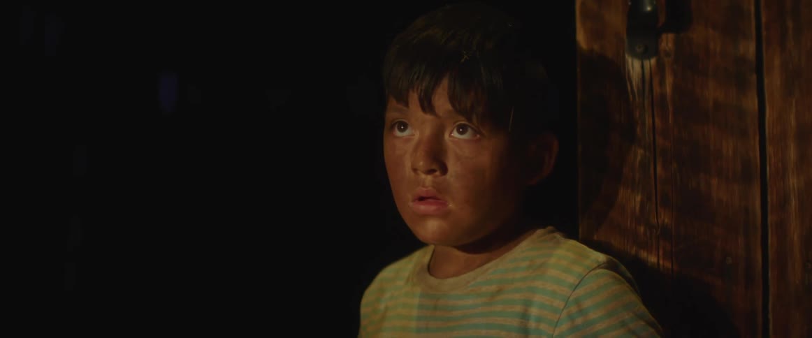A little boy with dirt all over his face walks through a door