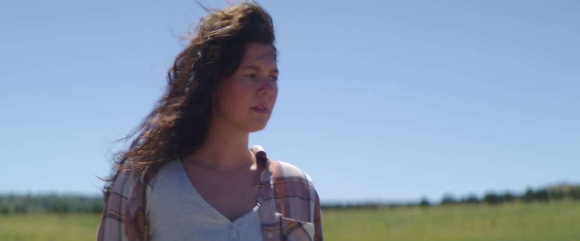Mother with wavy hair and a striped shirt holding her sons hand walks in an open field on a windy day