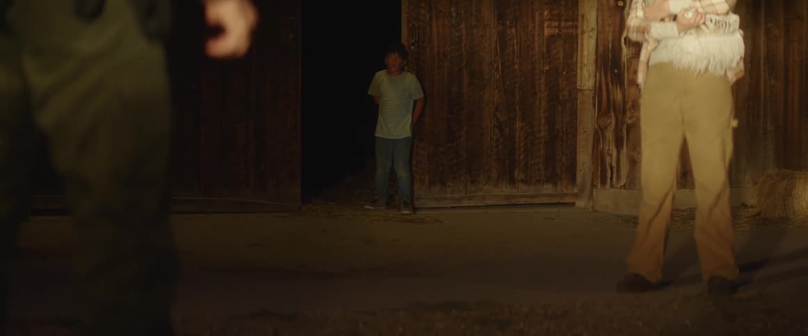 A little boy walks in to a barn with two people facing one another