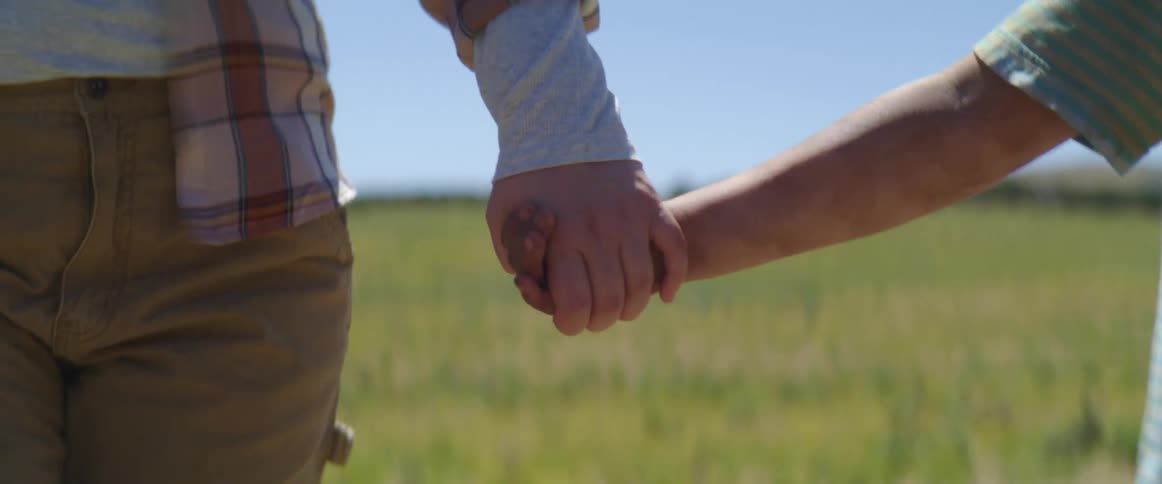 Adult and child walk on a grass field holding hands in a windy day