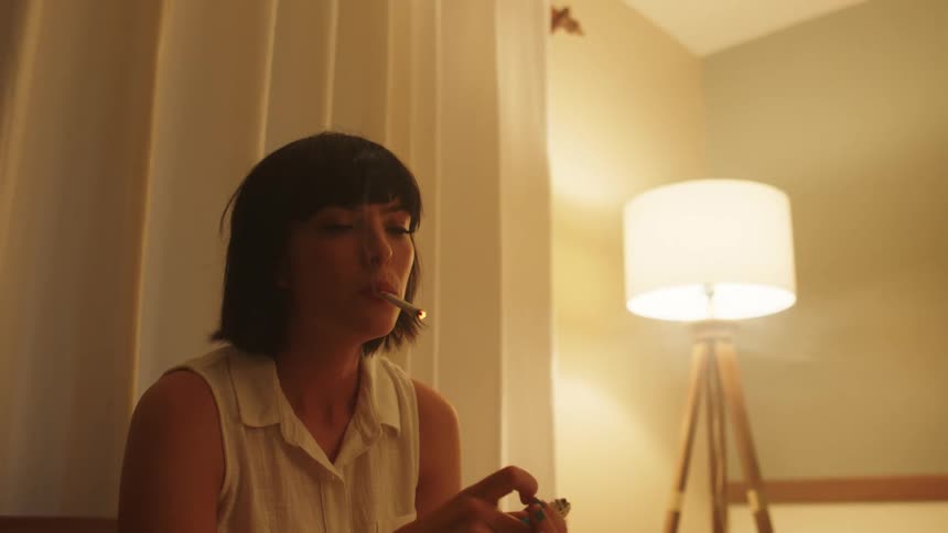 Woman sits near window lighting cigarette and smoking