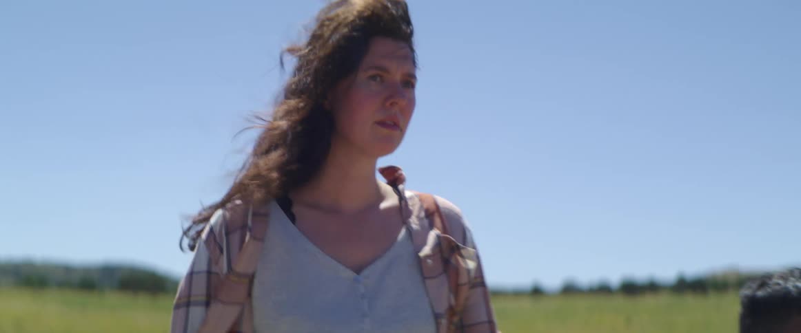 Mother with wavy hair and a striped shirt holding her sons hand walks in an open field on a windy day