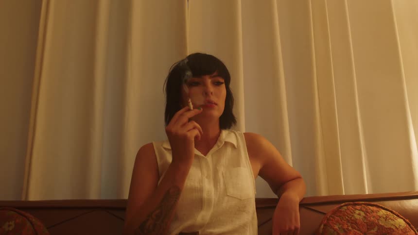 Woman smoking a cigarette sitting in a couch in a dimly lit room