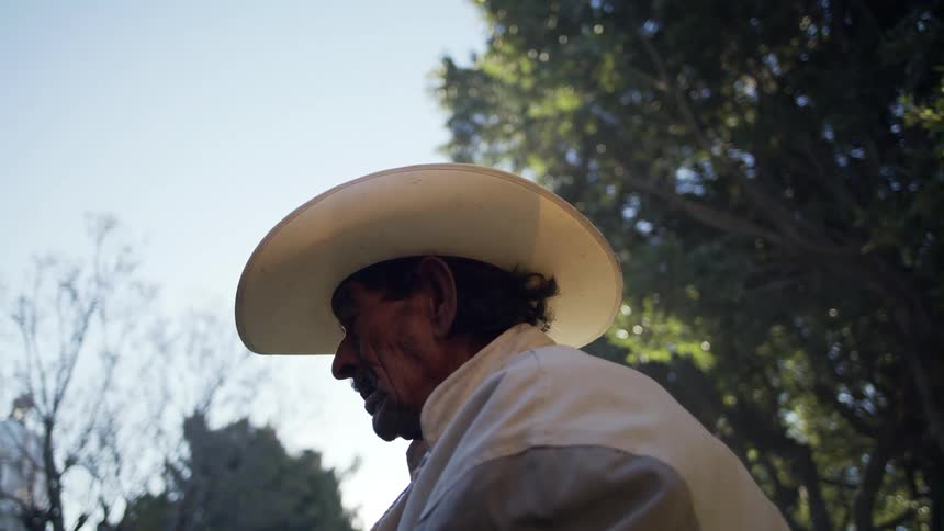 An aging man in a cowboy hat sits outside lost in thought as cigarette smoke swirls around him