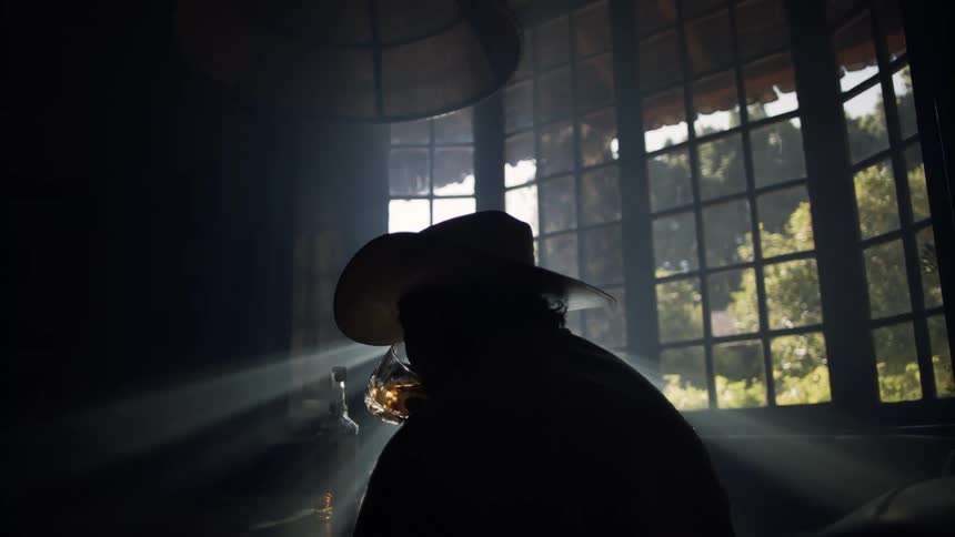 A man is having a drink in his dark living room