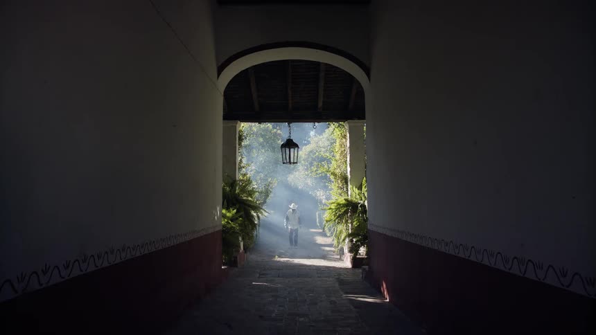 An older man in a cowboy hat walks through a large garden entryway of a private residence