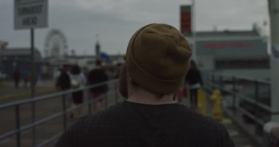 Man wearing a cap walking down a beach side area on a cloudy day