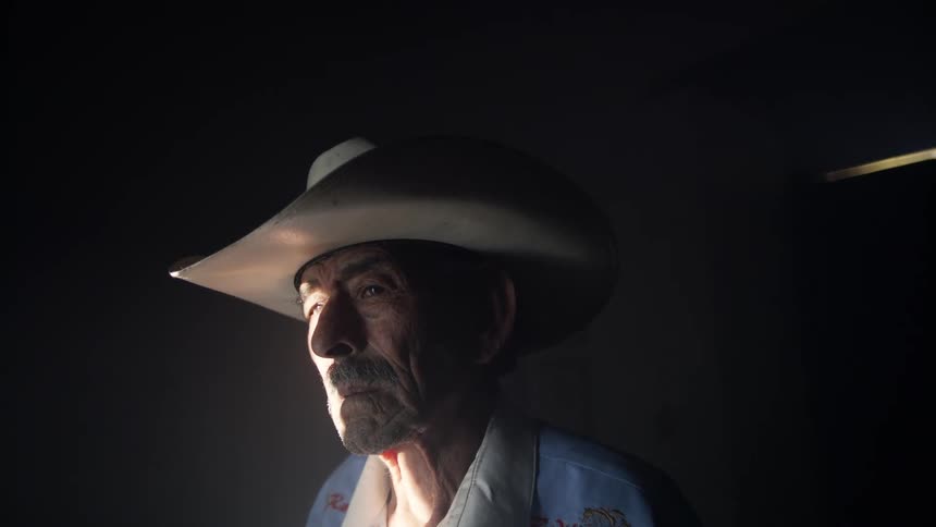 An elderly man in the darkness and then some light shines on him