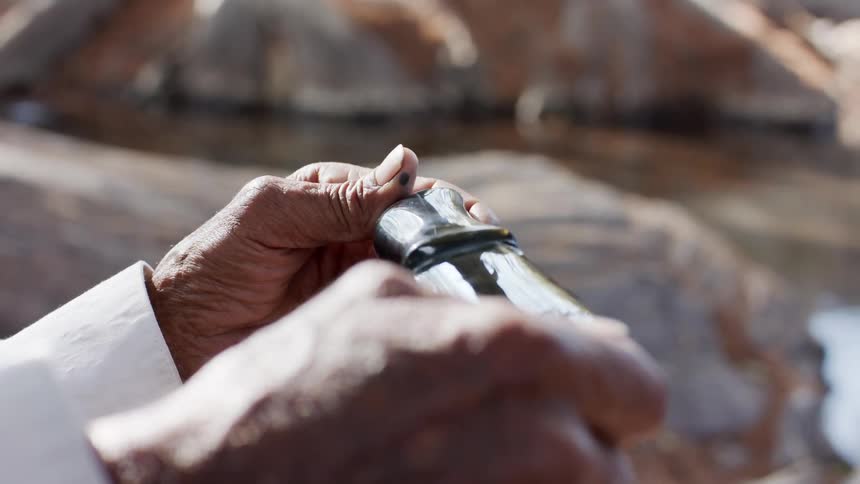 Person examines gloss stone on riverbank near flowing water
