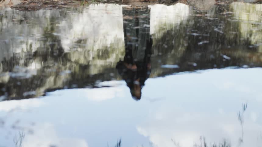 A woman looks at her reflection in the water