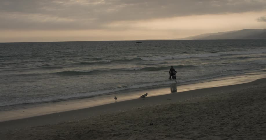 Two people wading in the surf at dusk or dawn
