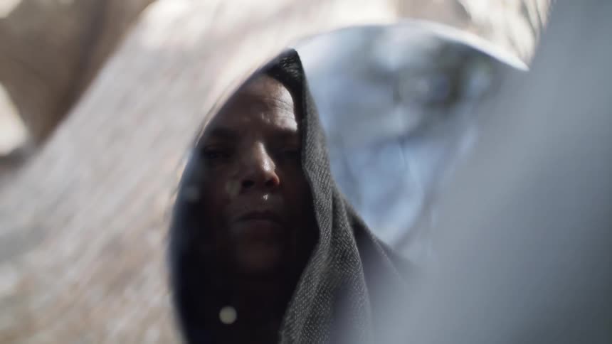 Man wearing a hood looks at his reflection in a mirror