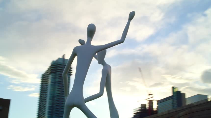 An outdoor sculpture of two pale humanoid figures in a metropolis on a sunny day