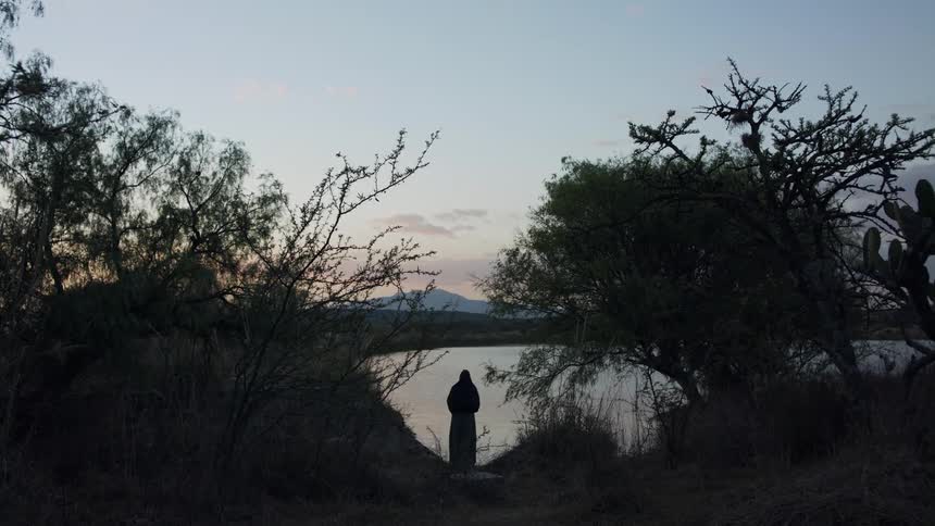 Woman stands by lakeside and is silhouetted against the lake at dusk