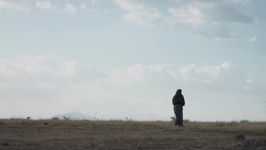 A woman walks across a bare field