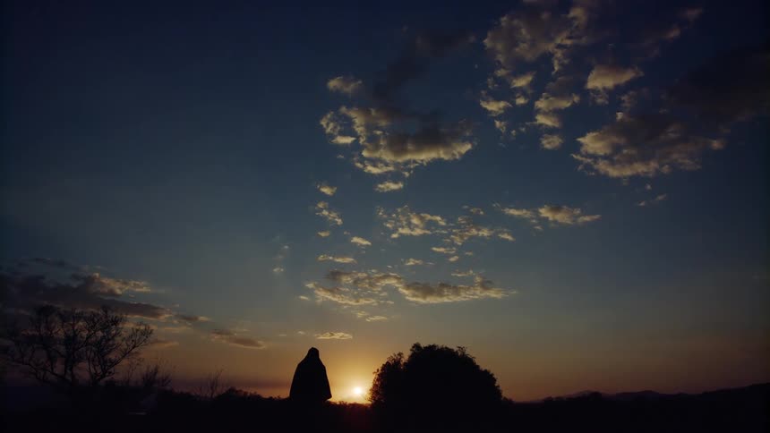 Silhouette of a woman wearing a robe walking through the desert at sunset
