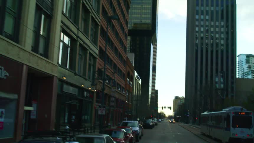 A commuter train travels on a city street near skyscrapers