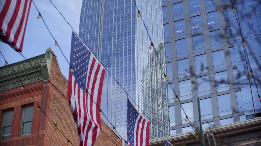 String lights and several american flags are hung across a street in a city