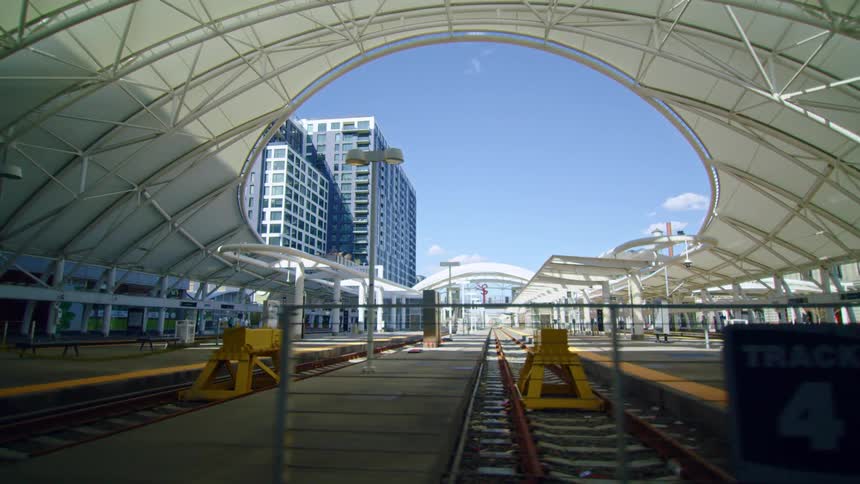 A train station with train tracks and a fence with buildings and the sky in the background