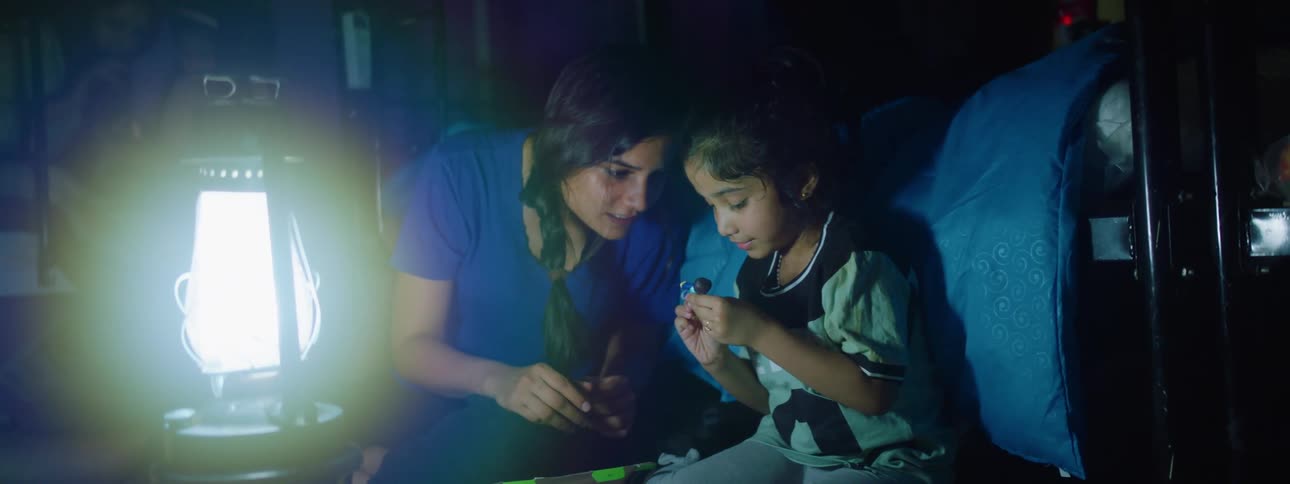 A mother and her daughter talk as they sit next to a lantern