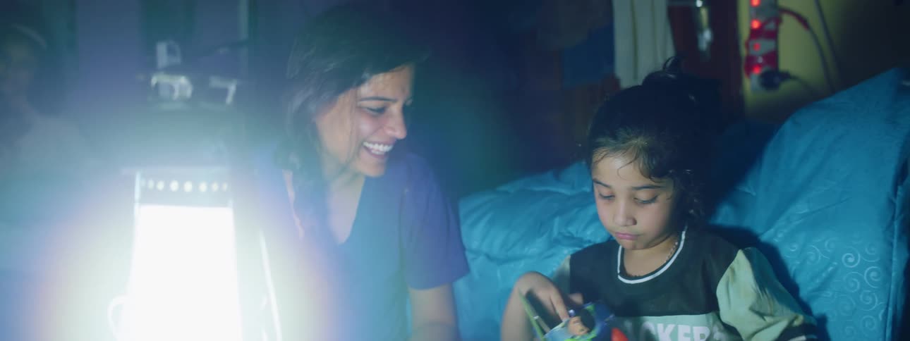 A child looks in a small box with a her mother sitting beside her on the floor