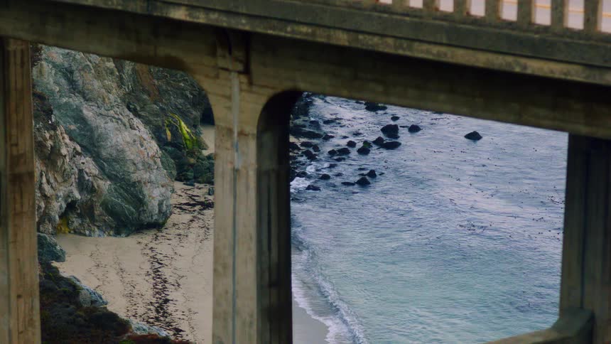 A bridge with pillars with a beach sand rocks and water underneath