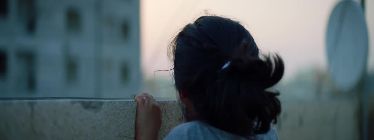 Girl stands looking over wall at apartment building